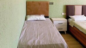 A bedroom with two beds, a nightstand, and a wall-mounted heater. - Empati Otel (Ayvalık)