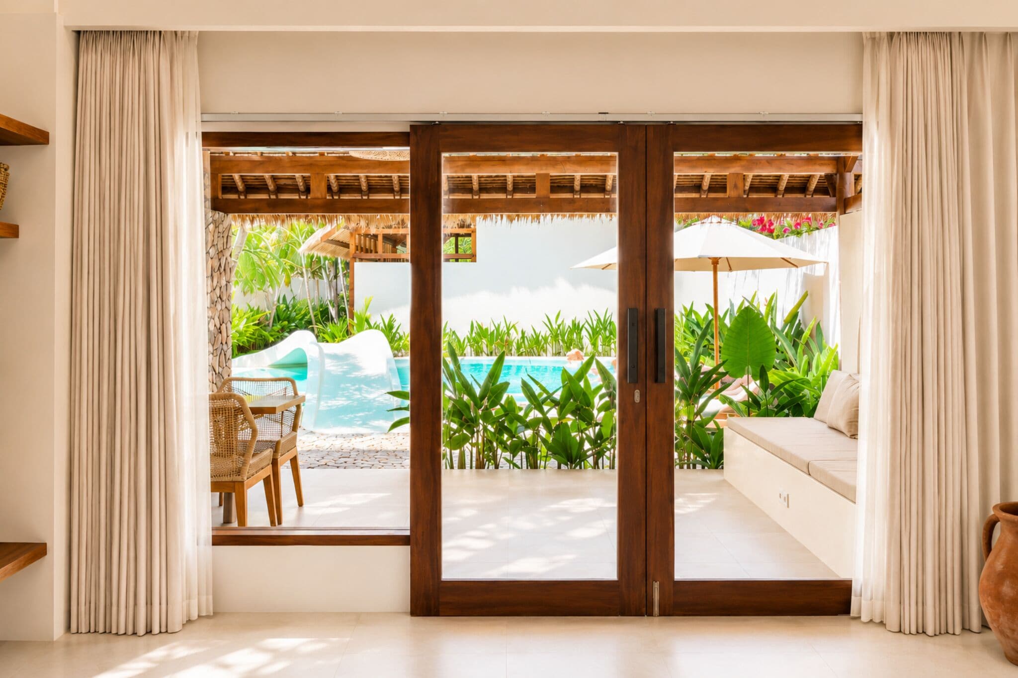Una habitación con puerta corrediza de vidrio que da a una zona de piscina, un sofá y una mesa con sillas.