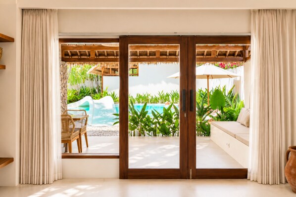 A room with a sliding glass door leading to a pool area, a sofa, and a table with chairs.