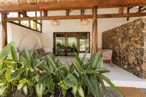 A covered outdoor area with a stone wall, a wooden pergola, and a seating area with a table and chairs. - ZENARA lombok - Boutique Adults Only (Kuta)