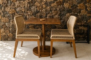 Una mesa redonda de madera con dos sillas de mimbre, frente a una pared de piedra.