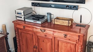 Ein Holzkabinent mit einem flachbildfernseher darüber, ein kleiner Tisch mit einer Kerze und ein Blumentopf.