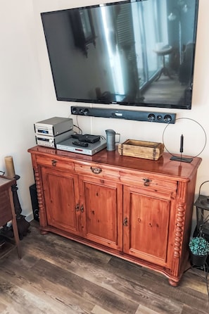A wooden cabinet with a flat-screen TV mounted above it, a small table with a candle, and a potted plant.