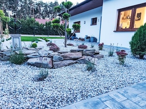 A modern house with a stone garden, a well-maintained lawn, and a visible kitchen window.