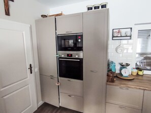 A kitchen with a built-in oven and microwave, a white door, and a countertop with various kitchen items. - Lesńy Kąt by Interhome (Stajenczynki)