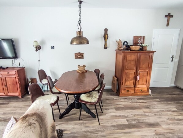 A dining area with a round table, chairs, a wooden cabinet, and a television on the wall.