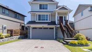 A two-story residential building with a garage, a stone retaining wall, and a small front yard with landscaping.