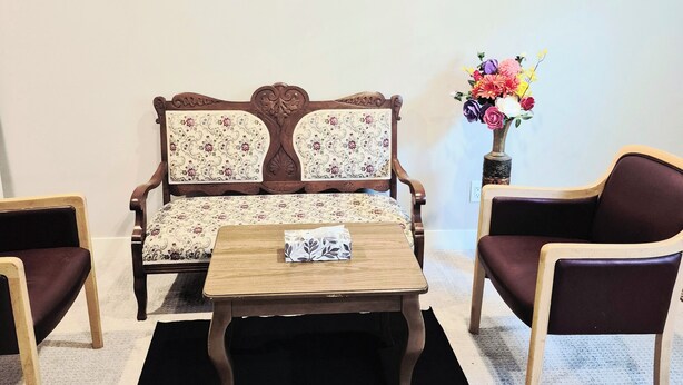 A room with a sofa, two armchairs, a coffee table, and a vase with flowers.