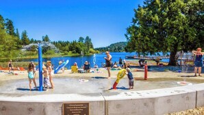 A water play area with a plaque, surrounded by a lake and trees.