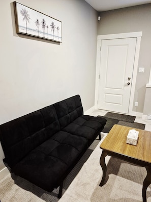 Una sala de estar con un sofá negro, una mesa de centro de madera y un cuadro en la pared.