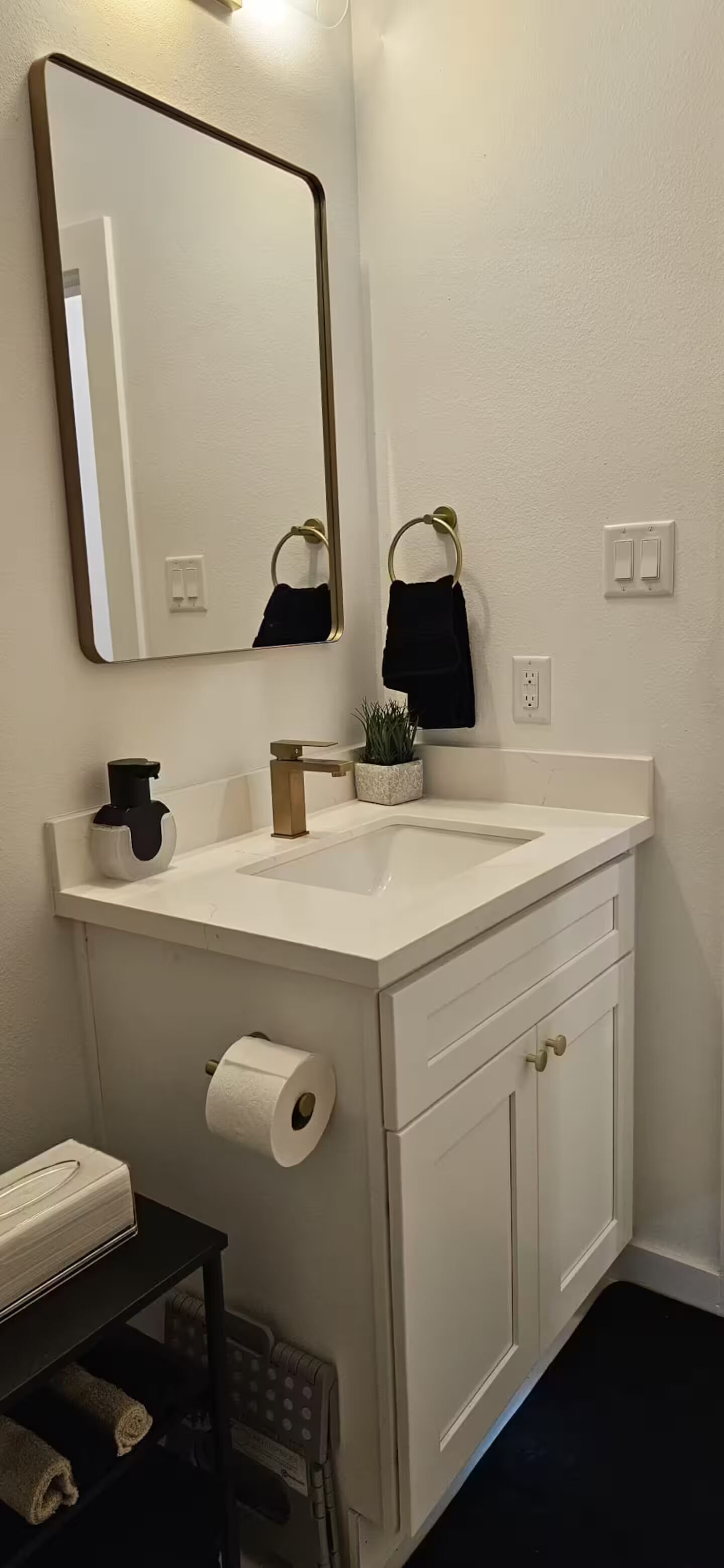 A bathroom with a white sink, a mirror, a towel rack, a toilet paper holder, and a small shelf with a towel.