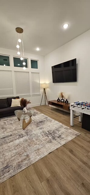 A modern living room with a sofa, a coffee table, a rug, a TV, and a foosball table.