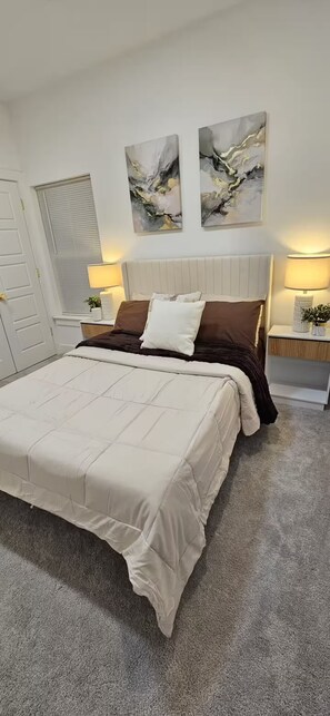 A bedroom with a large bed, two bedside tables, a headboard, and abstract wall art.