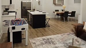 A modern kitchen with a central island, a dining area with a table and chairs, and a foosball table.