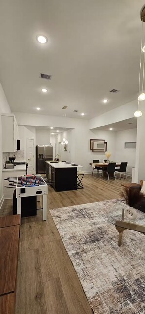 A modern kitchen with a central island, a dining area with a table and chairs, and a foosball table.