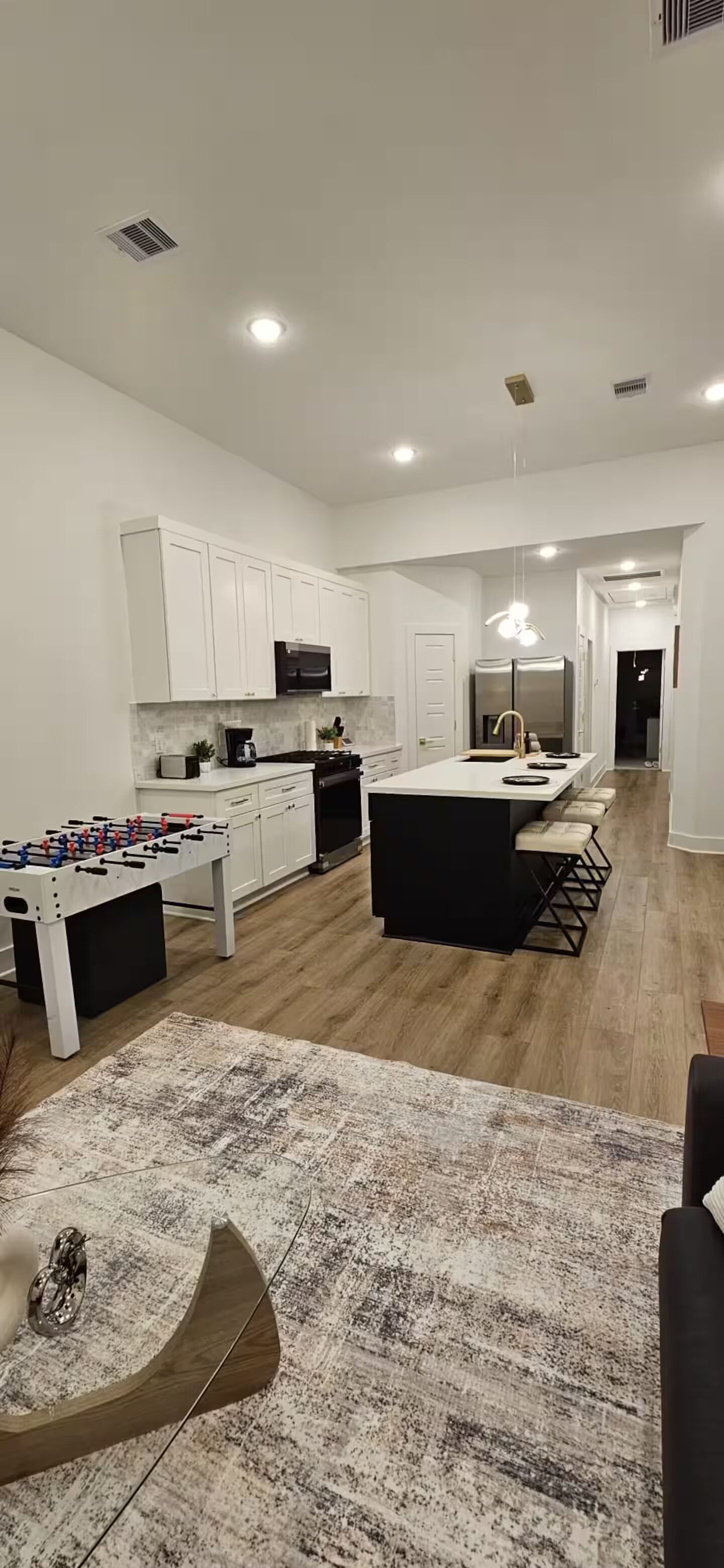 A modern kitchen with white cabinets, a central island, and a foosball table.