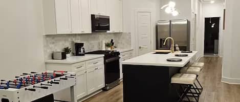 A modern kitchen with white cabinets, a central island, and a foosball table.
