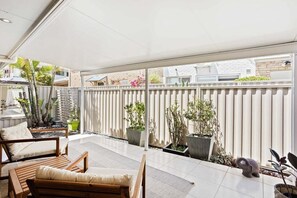 A covered patio with a wooden bench, potted plants, and a view of neighboring buildings. - Relax at Riviera - Villa in Miami (Gold Coast)