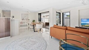 A modern living room with a sofa, a TV, and a dining area with a table and chairs. - Relax at Riviera - Villa in Miami (Gold Coast)