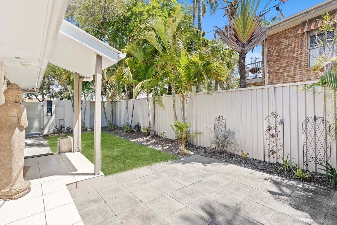 A backyard with a patio, a white fence, and various plants.