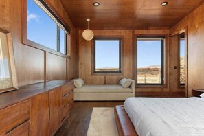 A bedroom with a wooden ceiling, a bed, a sofa, a dresser, and large windows offering a view of the landscape. - The Moki House (with hot tub) (Wayne County)