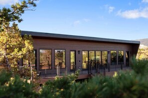 A modern building with large windows, a wooden deck, and a mountainous backdrop. - The Moki House (with hot tub) (Wayne County)