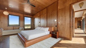 A bedroom with a large bed, wooden walls, a ceiling fan, and a view of the desert. - The Moki House (with hot tub) (Wayne County)