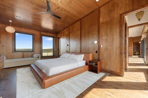 Ein Schlafzimmer mit einem großen Bett, Holzwänden, einem Deckenventilator und Blick auf die Wüste.