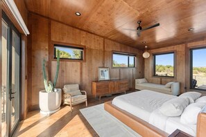 Ein Schlafzimmer mit einem großen Bett, Holzboden, Deckenventilator und einem Fenster mit Blick ins Freie.
