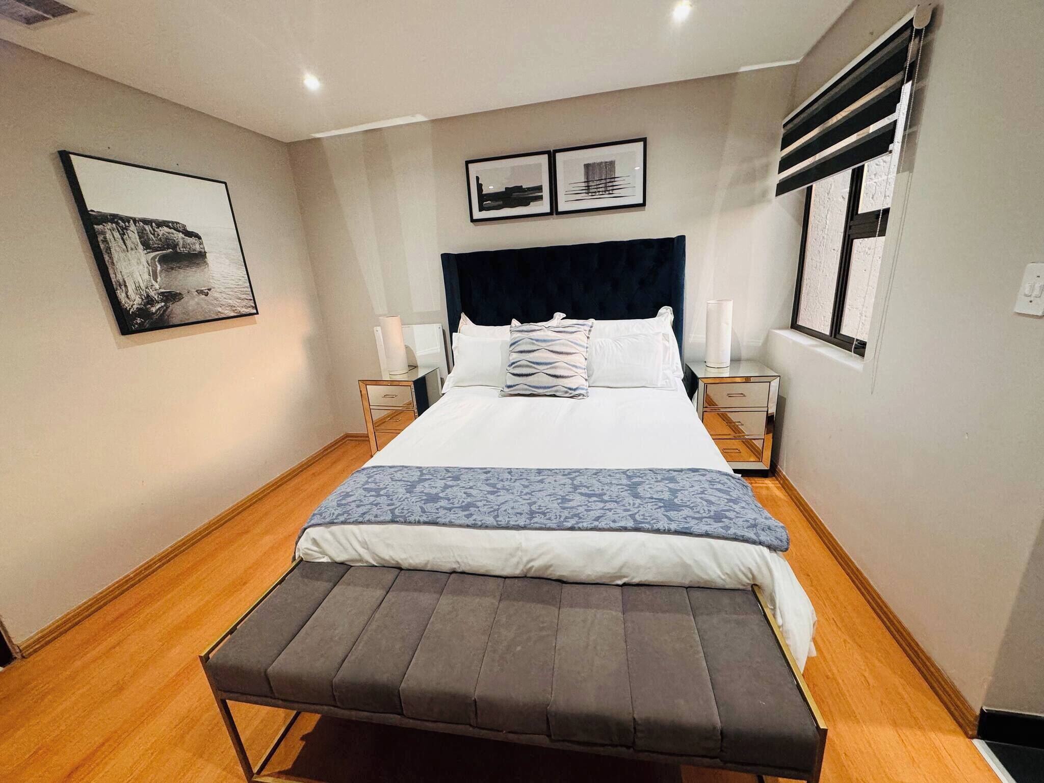 Un dormitorio ordenado con cama, mesitas de noche, un banco y obras de arte en las paredes.