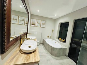 A modern bathroom with two sinks, a bathtub, and a large mirror.
