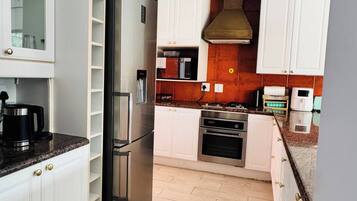A modern kitchen with white cabinetry, a stainless steel refrigerator, a built-in oven, and a microwave.