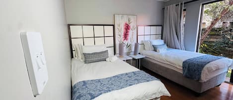 A hotel room with two beds, a large window, and a view of greenery outside.