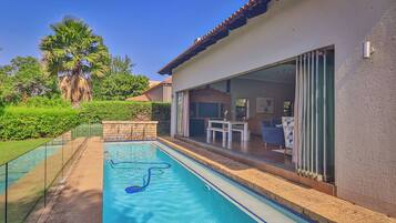 A swimming pool adjacent to a house with a sliding glass door leading to an outdoor patio.