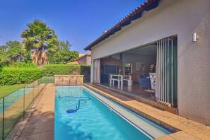 Une piscine située à côté d’une maison, avec une porte-fenêtre coulissante donnant sur un patio extérieur.