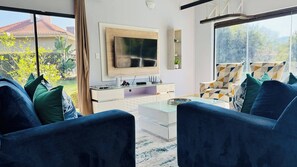 Een moderne woonkamer met een flatscreen televisie, een glazen salontafel en een bank met gekleurde kussens.