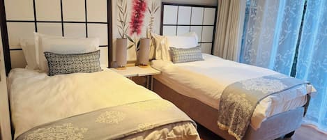 A hotel room with two beds, a nightstand, a painting, and sheer curtains.