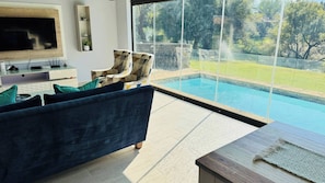 Una sala de estar moderna con un televisor grande, un sofá, un sillón y vista a una piscina.