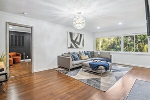 A modern living room with a grey sofa, a large abstract painting, and a chandelier. - Corporate Comfort | Stylish 3BR Extended Stay (Decatur)