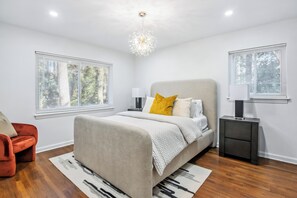 A modern bedroom with a large bed, a nightstand, a lamp, and a red chair. - Corporate Comfort | Stylish 3BR Extended Stay (Decatur)