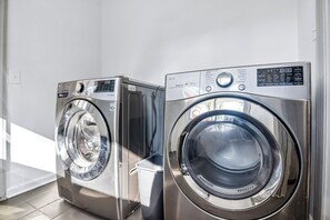 Two stainless steel front-loading washing machines in a room with white walls and a tiled floor. - Corporate Comfort | Stylish 3BR Extended Stay (Decatur)
