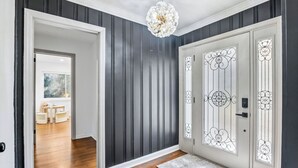 Un pasillo con paneles verticales oscuros, una puerta blanca con detalles de vidrio decorativo y una araña.