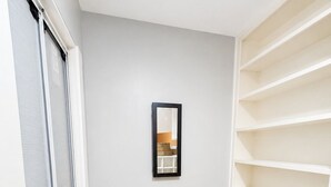 A room with a wooden floor, a white wall, and a black-framed mirror.