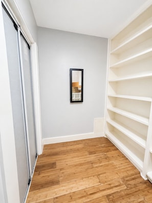 A room with a wooden floor, a white wall, and a black-framed mirror.
