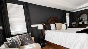 A bedroom with a bed, a chair, a nightstand, a mirror, and a window with blinds.