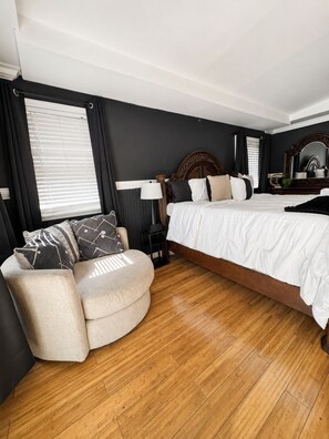 A bedroom with a bed, a chair, a nightstand, a mirror, and a window with blinds.