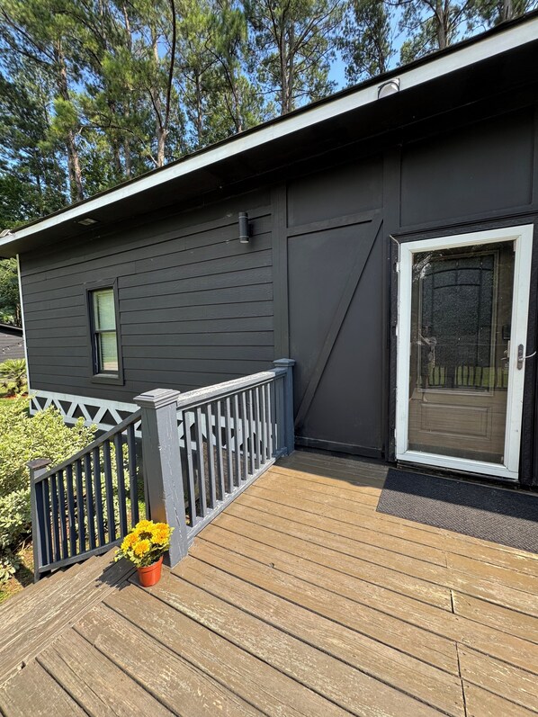 A dark-colored building with a wooden deck, a white door with a glass panel, and a small window.