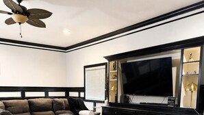 A modern living room with a sectional sofa, a coffee table, a flat-screen TV, and a ceiling fan.