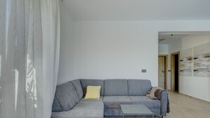 A modern living room with a grey sectional sofa, a small side table, and a wooden floor. - Vacation home  by Interhome (Krneza)