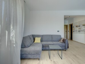 A modern living room with a grey sectional sofa, a small side table, and a wooden floor. - Vacation home  by Interhome (Krneza)